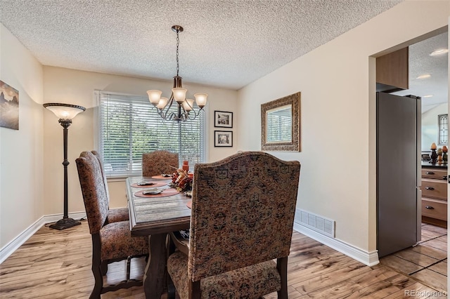 dining space featuring a textured ceiling, a chandelier, light wood-style floors, and baseboards