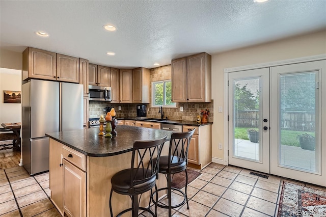 kitchen with appliances with stainless steel finishes, dark countertops, decorative backsplash, a sink, and french doors