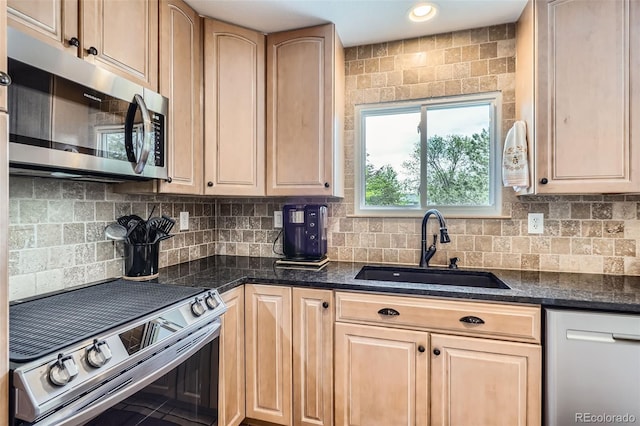 kitchen with stainless steel appliances, a sink, tasteful backsplash, and dark stone countertops