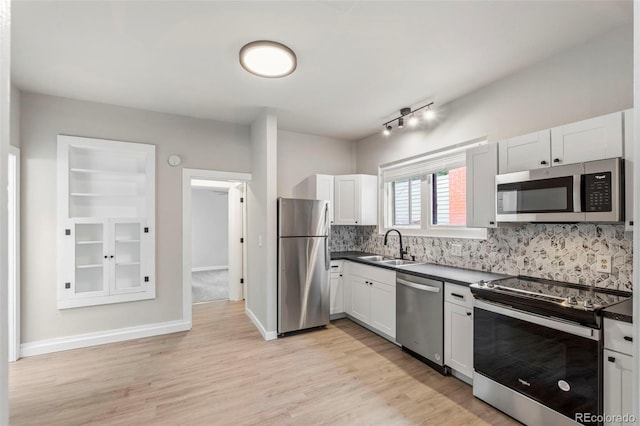 kitchen with stainless steel appliances, a sink, backsplash, light wood finished floors, and dark countertops