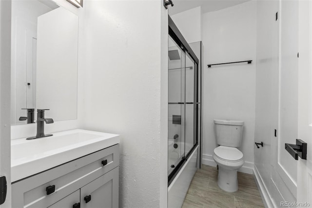 bathroom with toilet, baseboards, combined bath / shower with glass door, and vanity