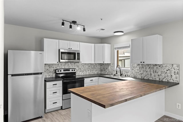 kitchen with white cabinets, wood counters, appliances with stainless steel finishes, a peninsula, and a sink