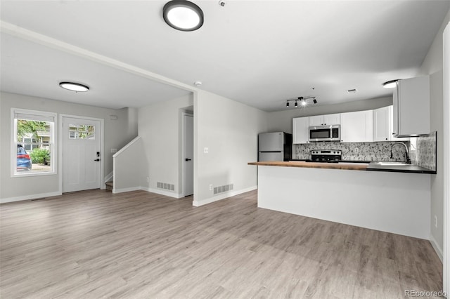 kitchen with stainless steel appliances, a sink, white cabinetry, light wood-type flooring, and tasteful backsplash