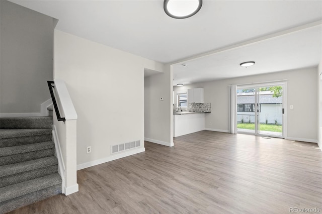 unfurnished living room featuring light wood-style flooring, a sink, visible vents, baseboards, and stairs