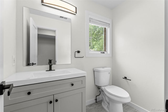 half bathroom with toilet, visible vents, baseboards, and vanity