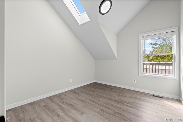 additional living space with lofted ceiling with skylight, visible vents, baseboards, and wood finished floors