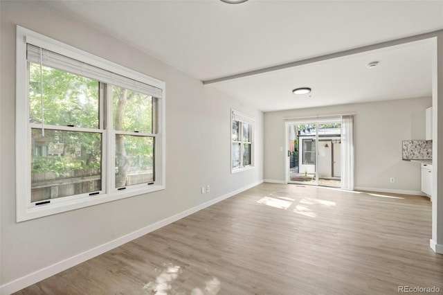 unfurnished room with wood finished floors, beam ceiling, and baseboards