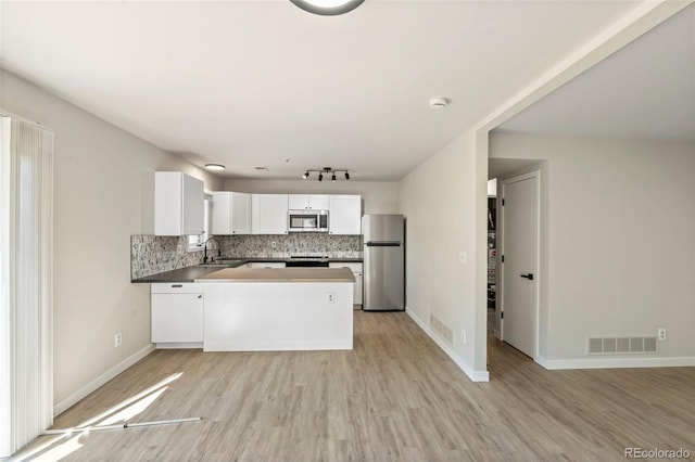 kitchen with a peninsula, visible vents, light wood-style floors, appliances with stainless steel finishes, and backsplash