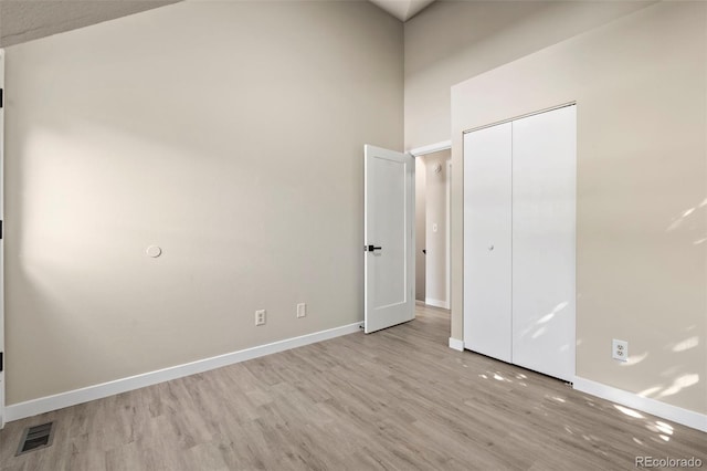 unfurnished bedroom with a closet, visible vents, a high ceiling, wood finished floors, and baseboards