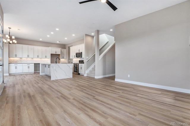 kitchen with white cabinetry, appliances with stainless steel finishes, a center island with sink, and light hardwood / wood-style flooring