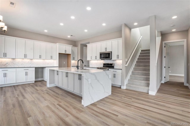 kitchen with light hardwood / wood-style floors, white cabinetry, sink, light stone counters, and appliances with stainless steel finishes