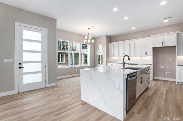 kitchen featuring stainless steel dishwasher, decorative light fixtures, a center island with sink, and white cabinets