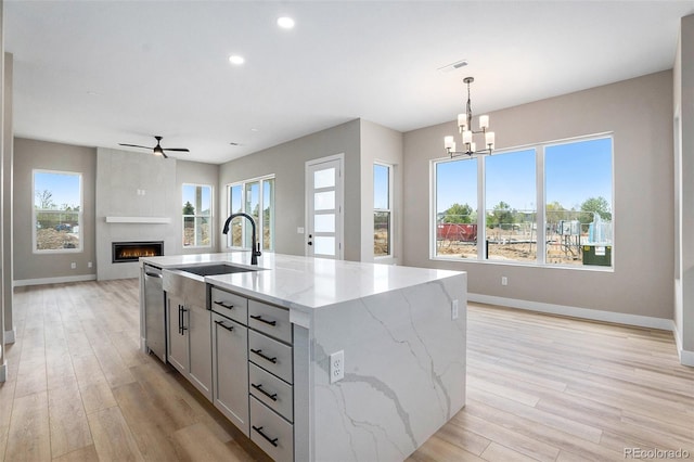 kitchen with hanging light fixtures, a healthy amount of sunlight, a center island with sink, and light stone counters