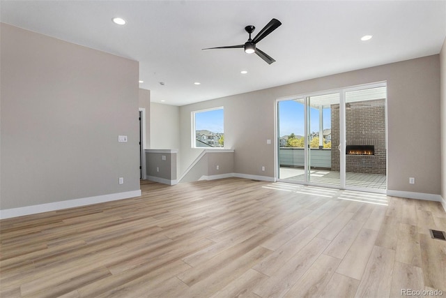 unfurnished living room featuring a fireplace, light hardwood / wood-style floors, and ceiling fan