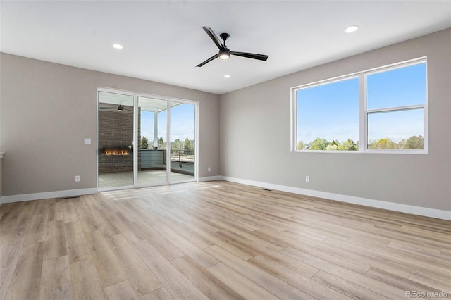 unfurnished room featuring a brick fireplace, light hardwood / wood-style floors, and ceiling fan