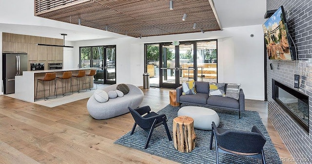 living room featuring a fireplace, brick wall, a wealth of natural light, and light hardwood / wood-style flooring