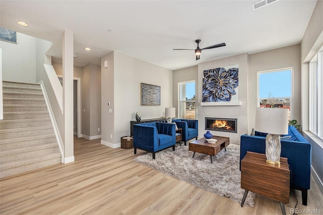 living area with stairs, light wood-type flooring, a wealth of natural light, and a fireplace