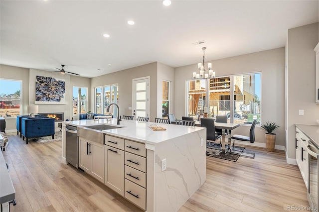 kitchen with light wood-style floors, a center island with sink, a lit fireplace, and a sink