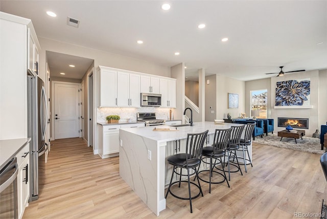 kitchen featuring visible vents, open floor plan, a breakfast bar area, appliances with stainless steel finishes, and a glass covered fireplace