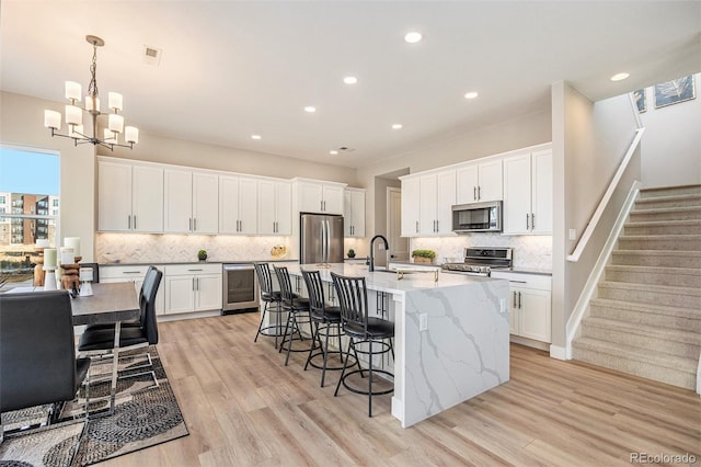 kitchen featuring a kitchen bar, a center island with sink, a sink, light wood-style floors, and appliances with stainless steel finishes