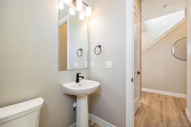 bathroom with toilet, wood finished floors, baseboards, and a textured wall