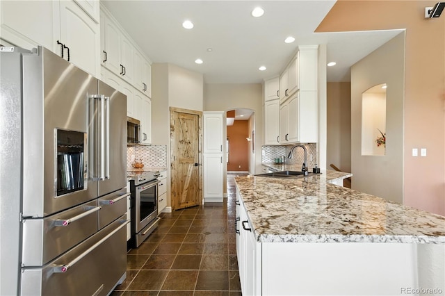 31200 E 145th Ave, Brighton, CO 80603 - kitchen with high end appliances, a peninsula, light stone counters, arched walkways, and white cabinetry