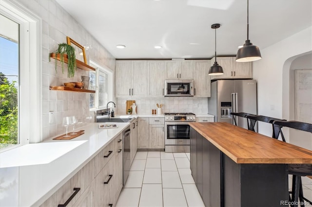kitchen featuring appliances with stainless steel finishes, a kitchen breakfast bar, butcher block counters, light tile patterned floors, and decorative backsplash