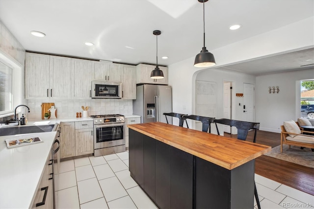 kitchen featuring appliances with stainless steel finishes, wooden counters, a sink, a breakfast bar area, and light tile patterned floors