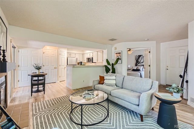 living room featuring a tiled fireplace, a textured ceiling, and light hardwood / wood-style flooring