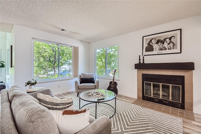 living room featuring light wood-type flooring, a textured ceiling, and a tile fireplace