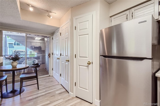 kitchen featuring stainless steel fridge, rail lighting, a textured ceiling, light hardwood / wood-style flooring, and white cabinetry