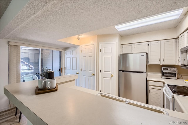 kitchen with stainless steel fridge, a textured ceiling, hardwood / wood-style floors, white electric range, and white cabinetry