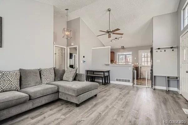 living area with light wood finished floors, baseboards, visible vents, a textured ceiling, and high vaulted ceiling