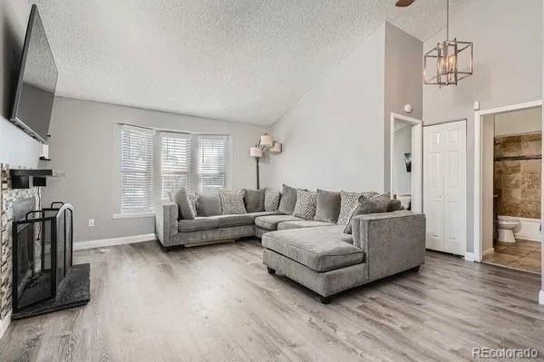 living room with a fireplace with raised hearth, a textured ceiling, wood finished floors, and lofted ceiling