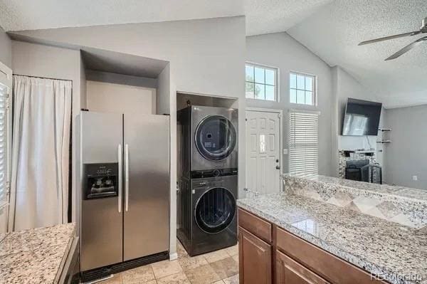 clothes washing area featuring laundry area, a textured ceiling, a ceiling fan, and stacked washer and clothes dryer