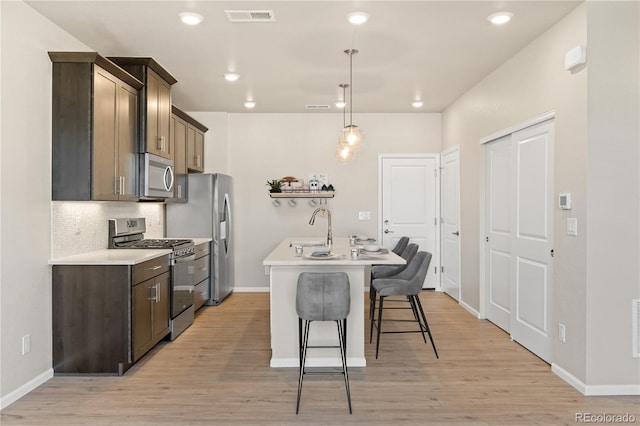 kitchen featuring pendant lighting, appliances with stainless steel finishes, a kitchen island with sink, a kitchen bar, and decorative backsplash