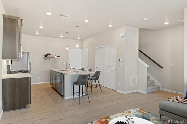 kitchen with sink, light hardwood / wood-style flooring, dishwasher, hanging light fixtures, and an island with sink