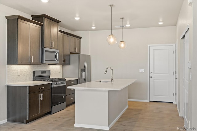 kitchen with sink, hanging light fixtures, stainless steel appliances, dark brown cabinets, and a center island with sink