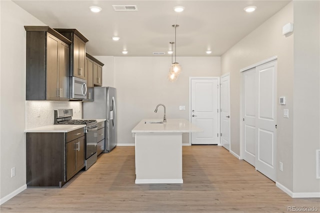 kitchen with sink, a kitchen island with sink, stainless steel appliances, decorative backsplash, and decorative light fixtures