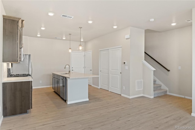 kitchen with pendant lighting, sink, a center island with sink, stainless steel dishwasher, and light wood-type flooring