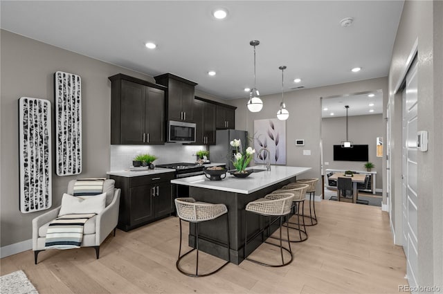 kitchen with freestanding refrigerator, a kitchen island with sink, light wood-type flooring, light countertops, and stainless steel microwave