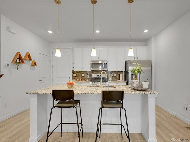 7488 W Pacific Ln, Denver, CO 80227 - kitchen with appliances with stainless steel finishes, white cabinets, a kitchen island with sink, light wood finished floors, and recessed lighting