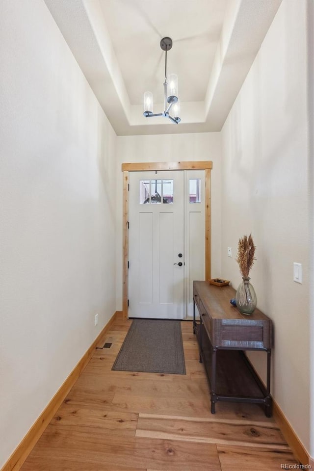 foyer entrance with an inviting chandelier, wood-type flooring, and a tray ceiling