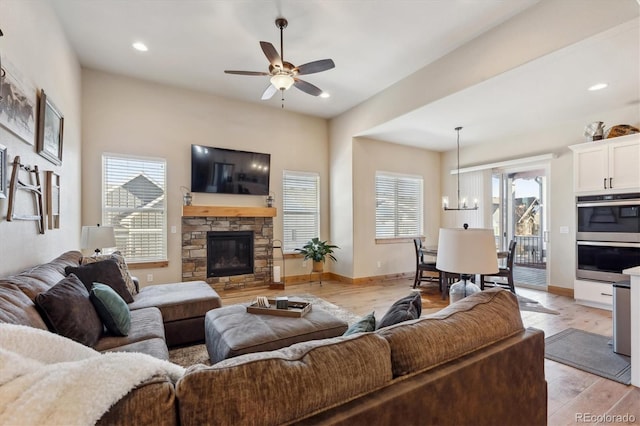 living room with a healthy amount of sunlight, ceiling fan with notable chandelier, a fireplace, and light hardwood / wood-style floors