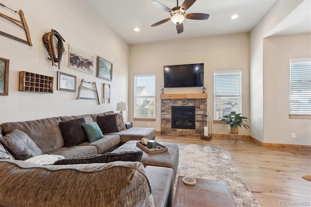 living room featuring ceiling fan, a stone fireplace, and light hardwood / wood-style flooring