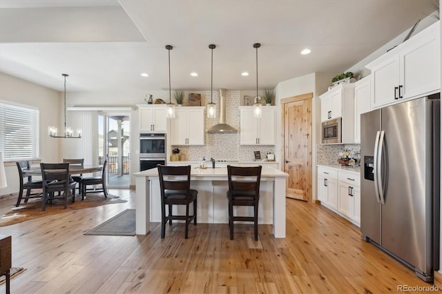 kitchen with wall chimney range hood, decorative light fixtures, white cabinets, and appliances with stainless steel finishes