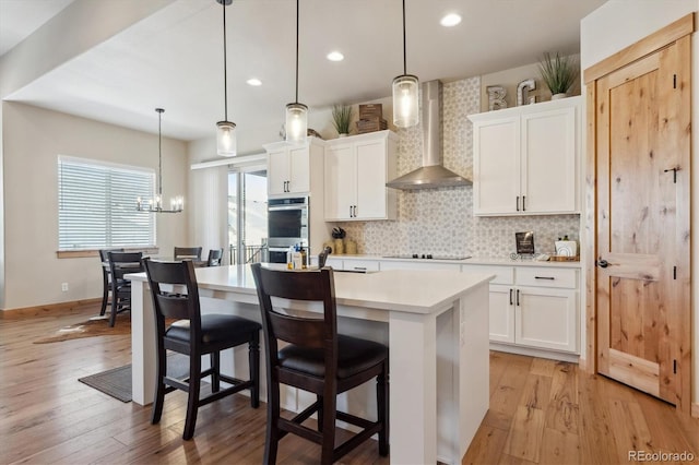 kitchen featuring pendant lighting, wall chimney range hood, and white cabinets