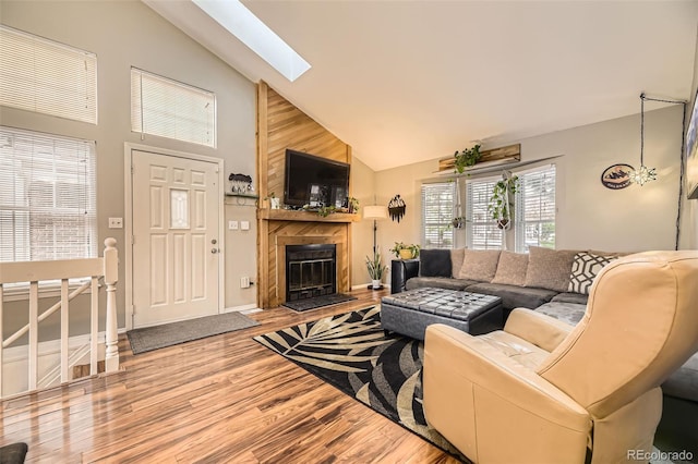 living room featuring a fireplace, wood finished floors, a skylight, and high vaulted ceiling