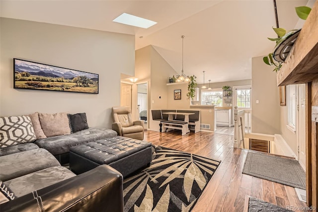 living area with visible vents, high vaulted ceiling, a skylight, and hardwood / wood-style flooring