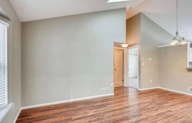 spare room featuring high vaulted ceiling, plenty of natural light, baseboards, wood finished floors, and visible vents